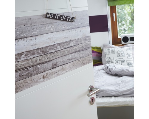 Teilansicht eines Zimmers mit geöffneter Tür, die mit einer Holzoptik-Tapete verziert ist und ein Schild mit der Aufschrift ''Do it often'' trägt