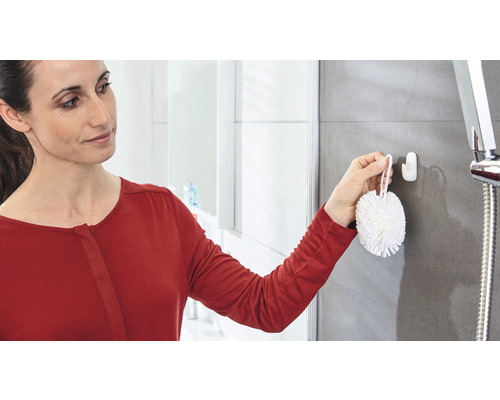 Frau befestigt einen Haken im Badezimmer für eine Duschbürste