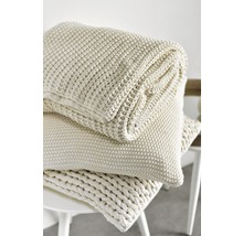 Gestapelte, gestrickte Tagesdecke und Kissen auf einem Hocker