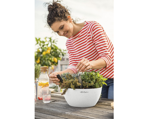 Frau pflanzt Kräuter in einem Blumentopf auf einem Holztisch im Freien.