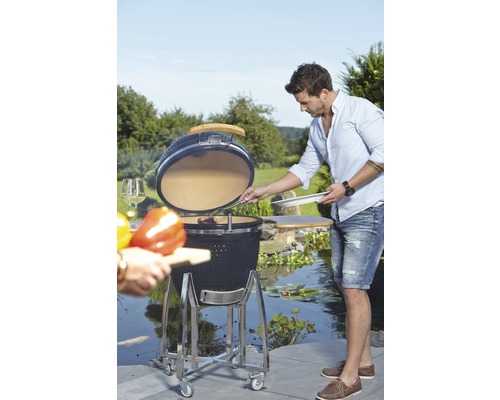 Keramikgrill auf Rollen mit offener Haube und Person beim Grillen