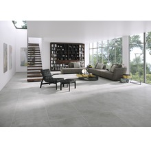 Helles Wohnzimmer mit grauen Bodenfliesen, Sofa, Bücherregal und Treppe
