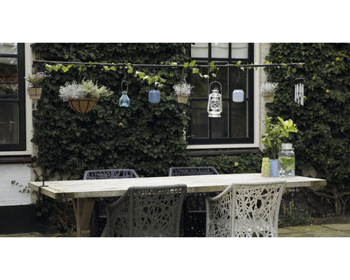 Gartenszene mit Holztisch, Stühlen und dekorativen Hängeelementen an einer mit Efeu bewachsenen Wand