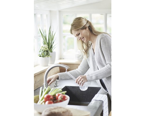 Femme à l''évier dans une cuisine lumineuse avec robinetterie et légumes frais