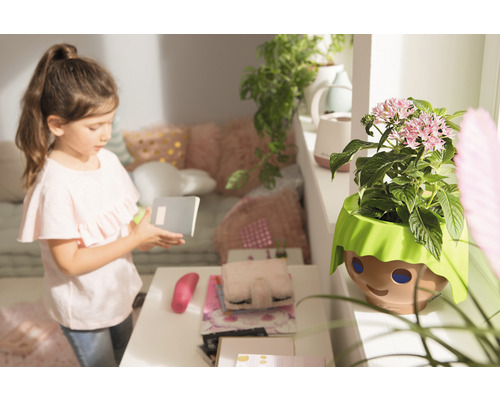 Mädchen mit Notizbuch neben Blumentopf mit Gesicht Design im Kinderzimmer.