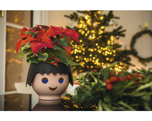Blumentopf in Form einer Playmobil-Figur mit Weihnachtsstern und Weihnachtsbaum im Hintergrund