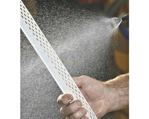 Un homme nettoie un profilé d''enduit perforé à l''aide d''un jet d''eau.