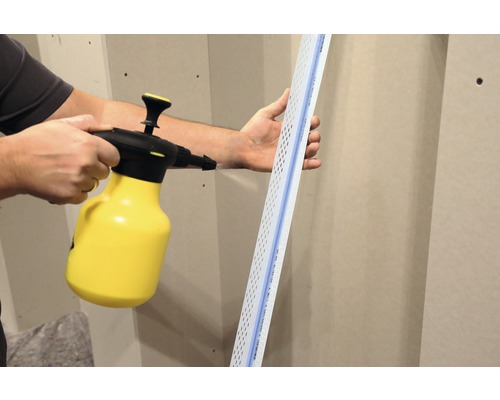 Une personne humidifie un profilé d''enduit à l''aide d''un pulvérisateur.