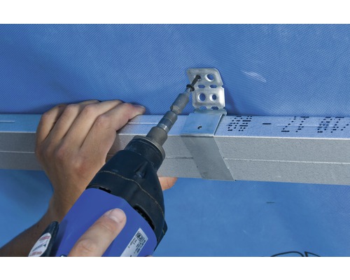 Un artisan fixe un rail métallique à un mur avec un tournevis.