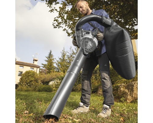 Un homme utilise un aspirateur de feuilles dans le jardin.