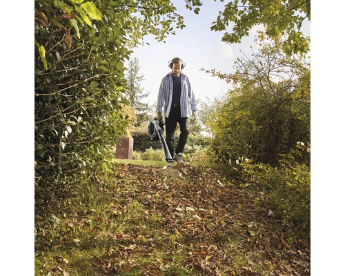 Homme avec souffleur de feuilles dans le jardin entre les buissons et les arbres