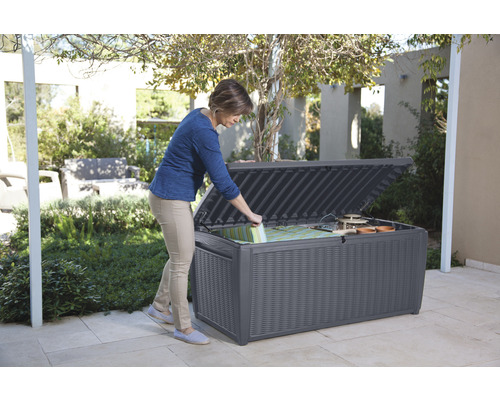 Femme ouvrant une boîte de rangement résistante aux intempéries dans le jardin pour coussins et outils de jardinage