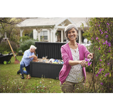 Frau schneidet Büsche im Garten mit einer Gartentruhe im Hintergrund