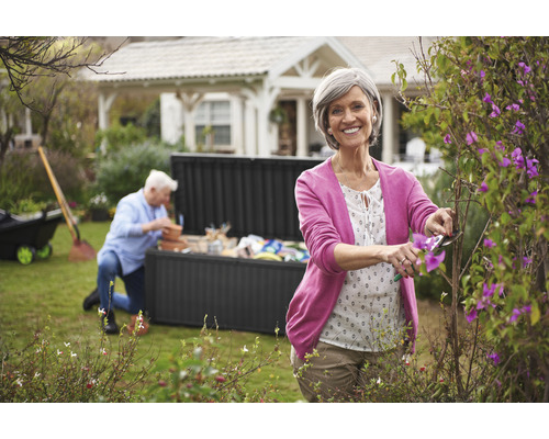 Femme taillant des buissons dans le jardin avec un coffre de jardin en arrière-plan