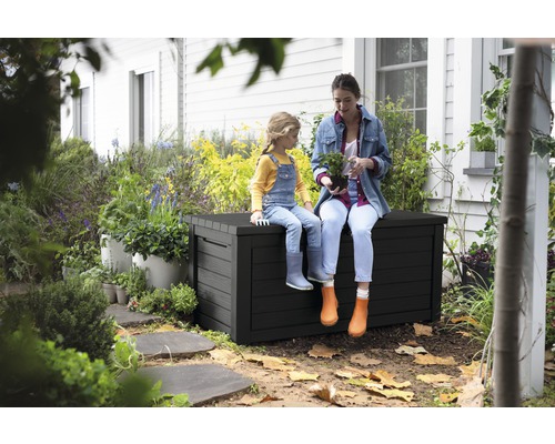 Eine Frau und ein Kind sitzen auf einer schwarzen Gartenbox im Garten.