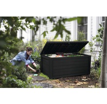 Gartenszene mit einer Frau, die neben einer geöffneten, schwarzen Gartenbox kniet