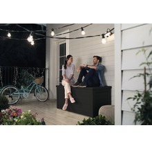 Ein Paar sitzt auf einer schwarzen Gartenbox auf einer Terrasse unter einer Lichterkette.