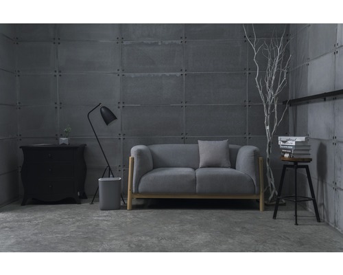 Graues Sofa mit Lampe, Kommode und Barhocker vor grauer Betonwand