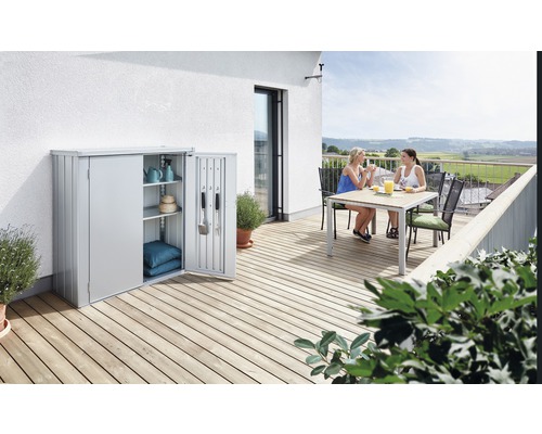 Graues Gerätehaus auf einer Terrasse mit zwei Frauen an einem Tisch