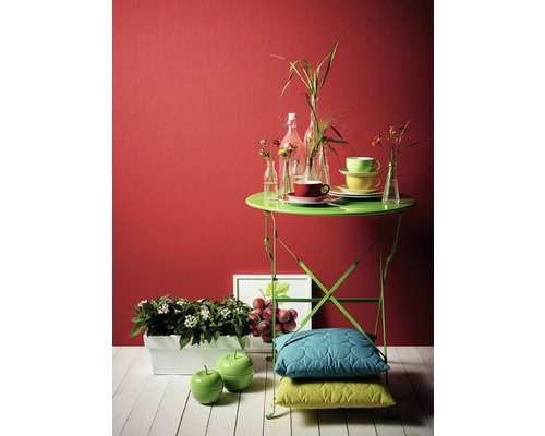 Dekorative Szene mit Gartentisch, Kissen, Blumen und Accessoires vor einer farbigen Wand