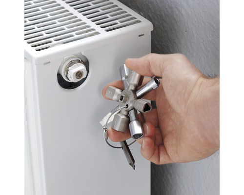 Une main actionne une clé de purge de radiateur sur un radiateur.