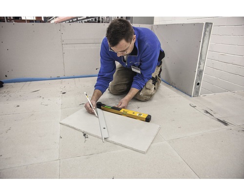 Eine Person zeichnet eine Linie mit einem Bleistift und einer Wasserwaage auf eine Gipskartonplatte.