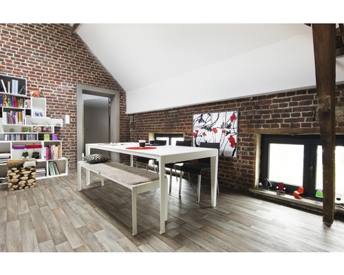 Salle à manger lumineuse avec table, banc, chaises et bibliothèque devant un mur en briques