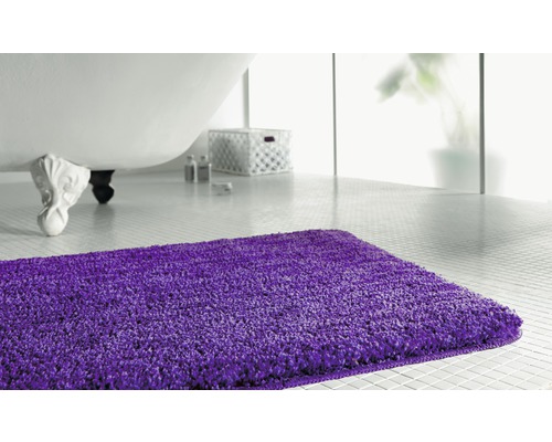 Lila Badteppich vor einer Badewanne in einem hellen Badezimmer.