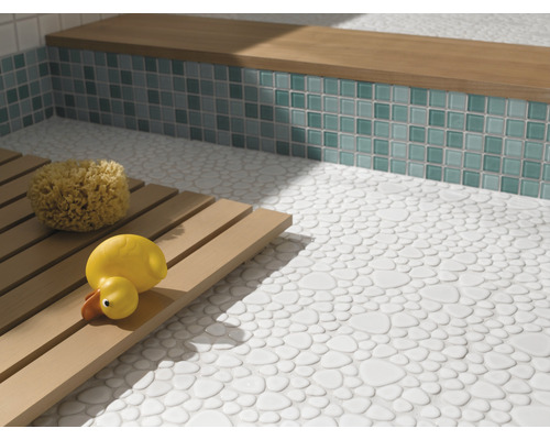 Badezimmer mit Boden aus Kieselsteinfliesen, Sitzbank mit Mosaikfliesen und Holzrost mit Badeschwamm und Quietscheente