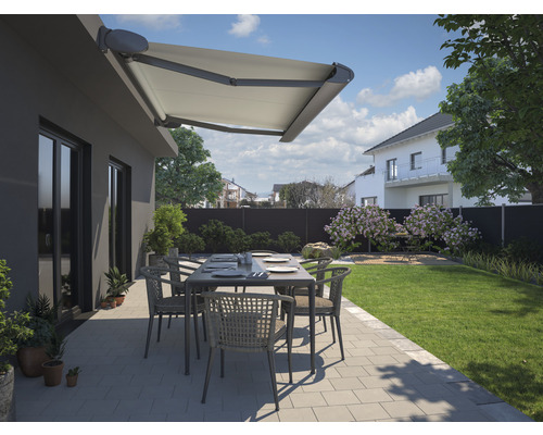 Terrasse avec store banne, table de jardin et chaises devant une maison.