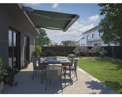 Terrasse avec store, table de jardin et chaises devant une maison.