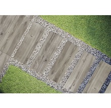 Scène de jardin avec des dalles de chemin en imitation bois, entourées de gravier et de gazon