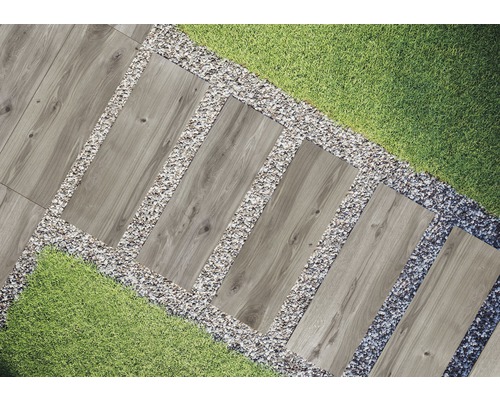 Scène de jardin avec des dalles de chemin en imitation bois, entourées de gravier et de gazon