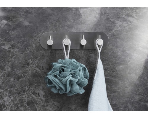 Wandgarderobe mit vier Haken aus Metall, daran hängen ein Badeschwamm und ein Handtuch.