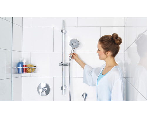 Frau stellt Handbrause an Duschstange im Badezimmer ein