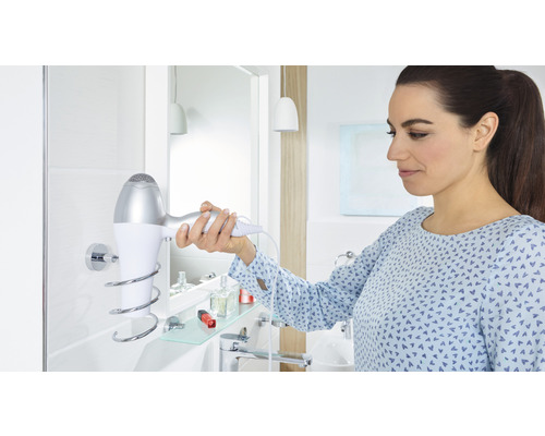 Frau nimmt Haartrockner aus Halterung im Badezimmer