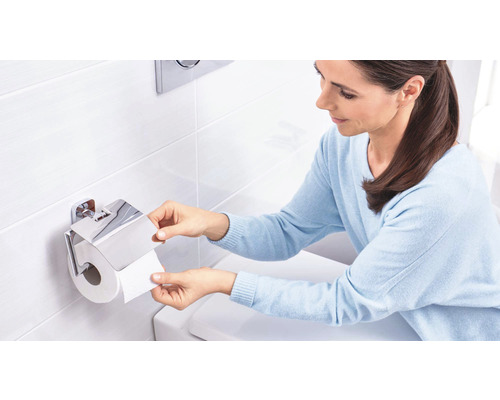 Une femme prend du papier toilette dans un support à papier toilette chromé avec couvercle.