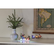 Scène décorative avec des branches de sapin dans un vase, une figurine de traîneau du Père Noël illuminée et une carte de l''Amérique du Sud.