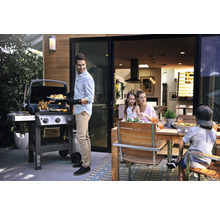 Une famille fait des grillades à l''extérieur avec un barbecue à gaz et une table à manger en bois.