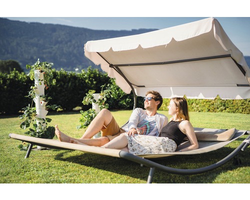Ein Paar entspannt auf einer Doppelliege mit Sonnendach neben einem Erdbeerturm im Garten.