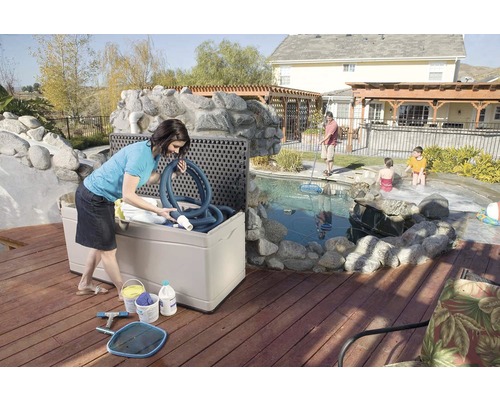 "Scène extérieure avec une femme remplissant un coffre de rangement pour accessoires de piscine sur une terrasse en bois près de la piscine 