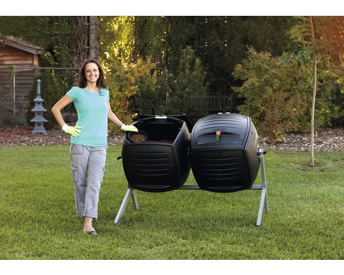 Une femme se tient à côté d''un composteur à tambour double noir dans le jardin.