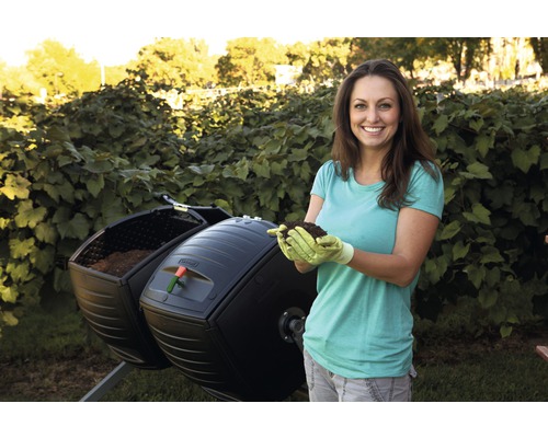 Une femme tient de la terre devant un composteur rotatif dans le jardin.