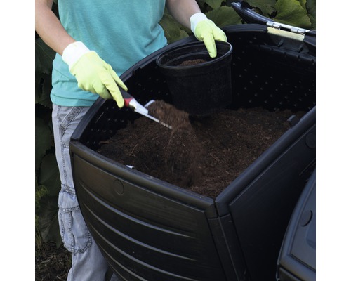 Une personne remplit un composteur de terre.