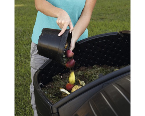Une personne vide des déchets organiques dans un composteur de jardin.