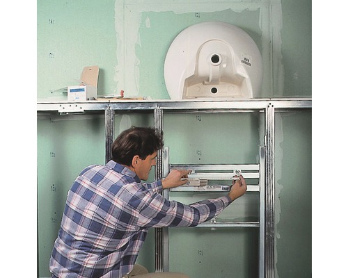 Un homme installe un bâti-support pour un lavabo dans la salle de bains.