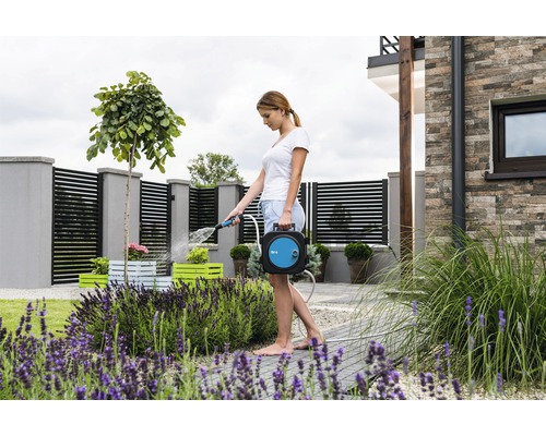 Une femme arrose des plantes avec un dévidoir dans le jardin.