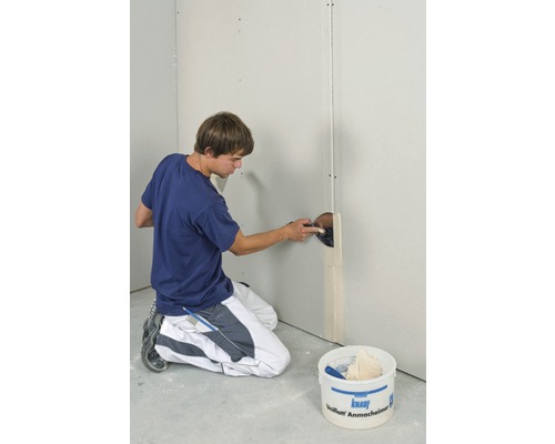 Un homme enduit un mur en plaques de plâtre avec du mastic dans un intérieur.