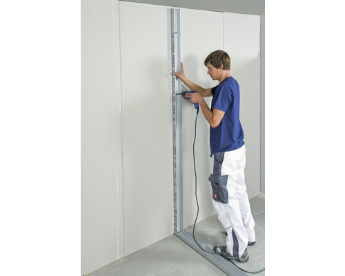 Un homme fixe une sous-construction métallique à un mur avec une visseuse.