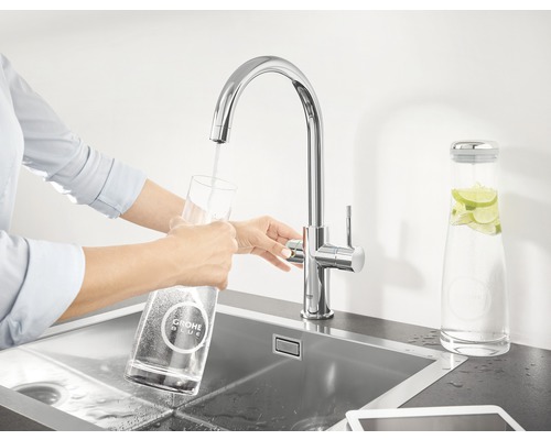 Femme remplissant un verre avec un robinet Grohe Blue dans un évier.